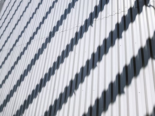 Clean white ribbed metal roof panels finished with a reflective acrylic roof coating in bright sunlight