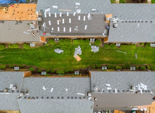 Aerial view of a residential neighborhood with visible storm damage across multiple roofs