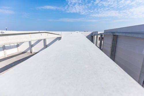 Bright white silicone roof coating applied across a commercial low-slope roof under a clear blue sky